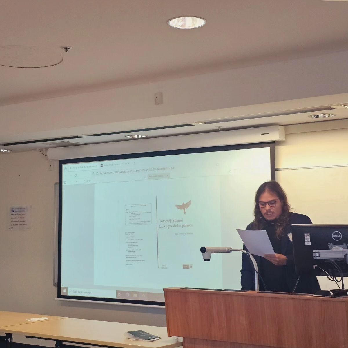 A conference presentation with La Lengua de los Pájaros projected on the screen